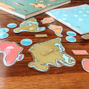 May include: A set of colorful world map stickers with labels for each continent. The stickers are on a wooden surface. The continents are labeled: North America, Asia, Africa, South America, Europe, Australia, and Antarctica.