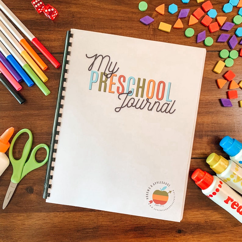 May include: A white journal with the words "My Preschool Journal" in colorful letters. The journal has a spiral binding and a colorful apple logo on the bottom.
