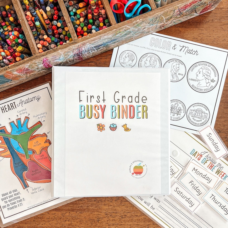 K&ouml;nnte beinhalten: Ein wei&szlig;er Ordner mit dem Text "First Grade Busy Binder" in bunten Buchstaben. Der Ordner hat einen roten Apfel mit einem gr&uuml;nen Blatt und einen wei&szlig;en Pfeil, der nach rechts zeigt. Es gibt auch drei kleine Illustrationen einer Blume, eines Vogelnests mit einem Vogel und einer gelben Gummiente.