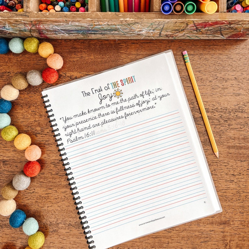 May include: A notebook with a white cover and a spiral binding. The cover has a colorful design with the words "The Fruit of the Spirit Joy" and a Bible verse: "You make known to me the path of life, in your presence there is fullness of joy, at your right hand are pleasures forevermore." Psalm 16:11 am 5:16-18