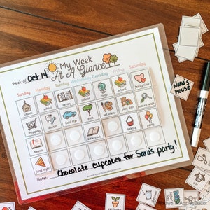 K&ouml;nnte beinhalten: Ein transparenter Wochenplaner aus Plastik mit gr&uuml;nem Rand und dem aufgedruckten Text "My Week At A Glance". Der Planer ist in Wochentage unterteilt, wobei jeder Tag ein Raster aus Feldern f&uuml;r Aktivit&auml;ten hat. Die Felder sind mit kleinen Bildern gef&uuml;llt, die verschiedene Aktivit&auml;ten darstellen, wie z. B. Kirche, Schule, Bibliothek, Park, Kunstunterricht, Verabredung, Spaziergang in der Natur, Backen und Party. Der Planer enth&auml;lt auch einen Notizbereich am unteren Rand.