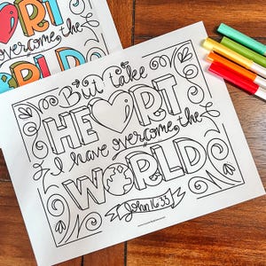 May include: Two white coloring pages with the words "But take heart, I have overcome the world" and "John 16:33" in black, outlined letters. The word "HEART" is in large, 3D letters. Colored markers in red, orange, yellow, green, and blue are visible.