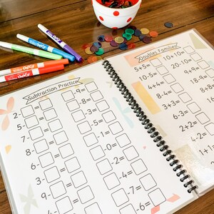 May include: A colorful workbook with subtraction practice problems on the left page and doubles families math problems on the right page. The workbook has a spiral binding and is open to show both pages.