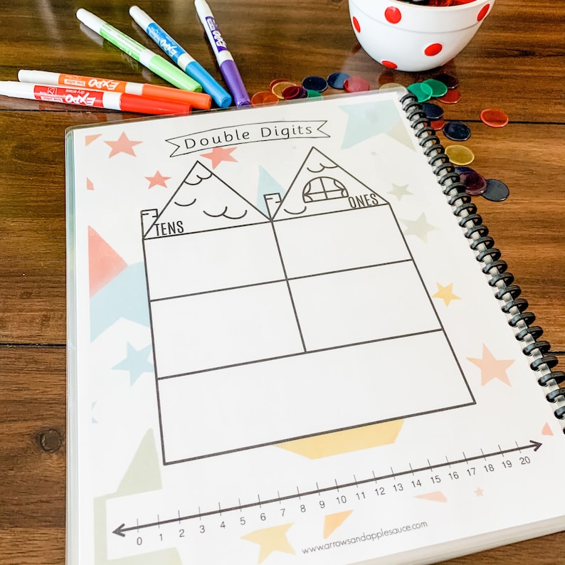 May include: A white page with a black and white illustration of a house divided into two sections labeled "Tens" and "Ones". The page is decorated with colorful stars and geometric shapes. A number line from 0 to 20 is at the bottom of the page.