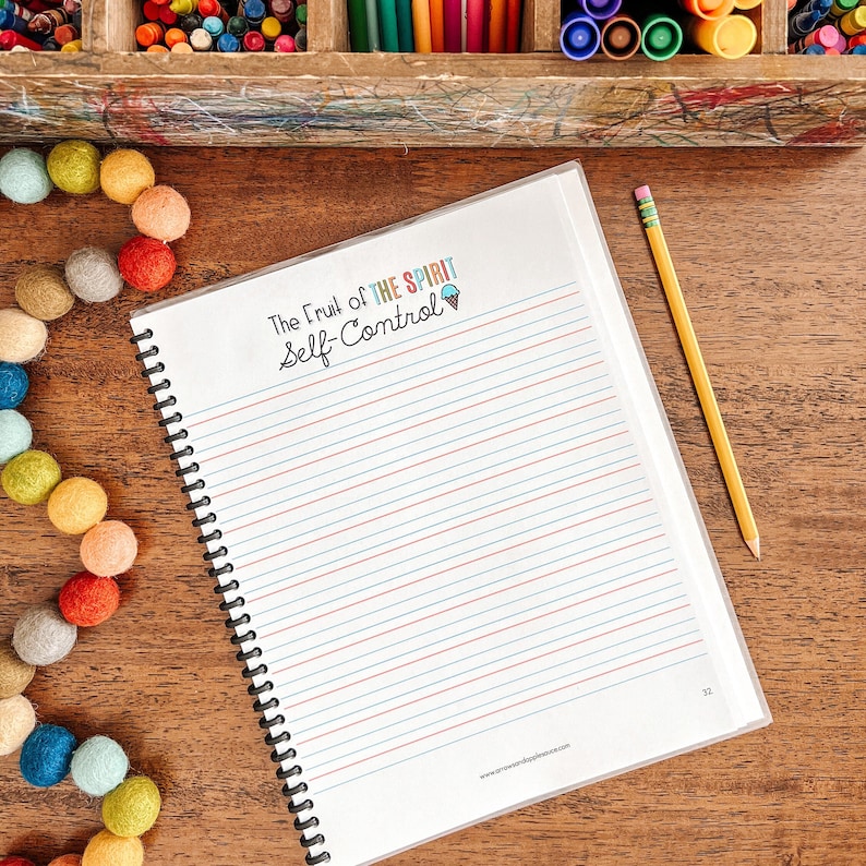 May include: A notebook with a white cover and a spiral binding. The cover has the text "The Fruit of the Spirit Self-Control" in colorful letters. The notebook has lined pages and is on a wooden surface.