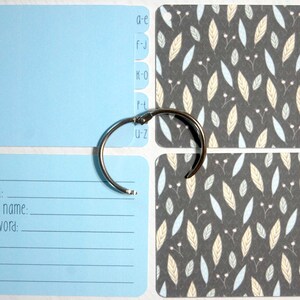 May include: A blue card holder with a ring binder and alphabetical tabs. The card holder has a blank card and a card with the text "email: user name: password:". The binder is decorated with cards featuring a pattern of light blue and yellow leaves on a gray background.