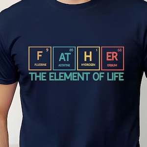 May include: Navy blue t-shirt with the word "FATHER" spelled out using periodic table elements. The text "THE ELEMENT OF LIFE" is below the word "FATHER". The shirt is a crew neck style.