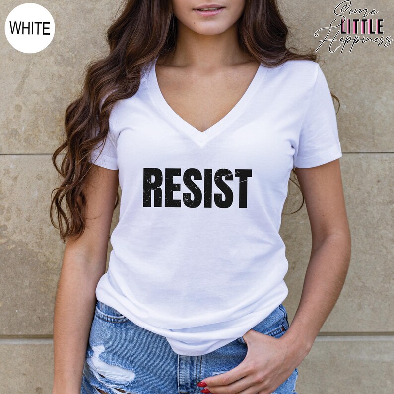 May include: White v-neck t-shirt with the word "RESIST" printed in black on the front.