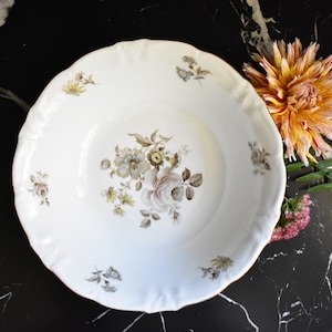 May include: A white porcelain bowl with a floral design in shades of brown and gray. The bowl has a scalloped edge and a gold rim.