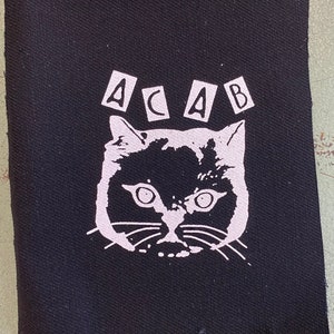 Peut inclure: Patch thermocollante noir et blanc avec un visage de chat et les lettres "ACAB" au-dessus.