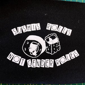 May include: Black fabric patch with white text that reads "Sushi's Rolls Not Gender Roles" and a graphic of two sushi rolls.