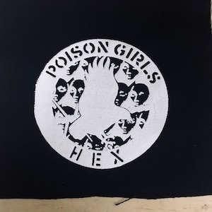 May include: White patch with a black background. The patch features a white circle with the text "POISON GIRLS HEX" and a stylized image of a bird with multiple faces surrounding it.