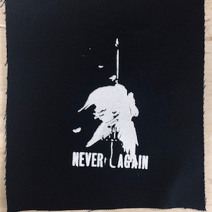Puede incluir: Parche de tela negro con una silueta blanca de una persona sosteniendo una espada y el texto "NEVER AGAIN".