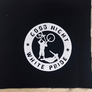 Peut inclure: Un patch noir avec un cercle blanc contenant le texte "Good Night White Pride" et une silhouette de deux personnes, l'une tenant un vélo au-dessus de sa tête.