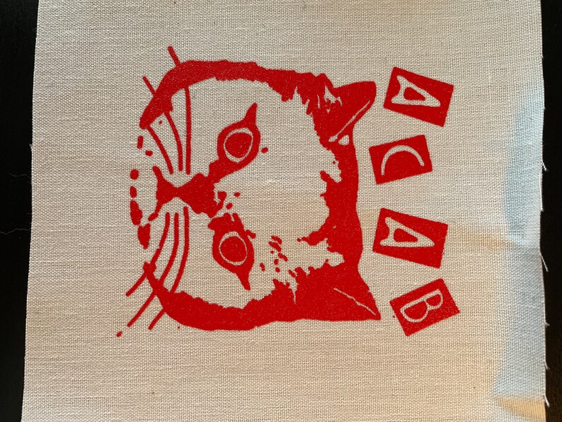 K&ouml;nnte beinhalten: Roter gestickter Aufn&auml;her mit einem Katzenkopf und den Buchstaben "ACAB" dar&uuml;ber.