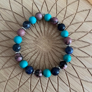 May include: A bracelet made of blue, turquoise, and pink stones with silver accents. The bracelet is made of natural stones and is a beautiful piece of jewelry.