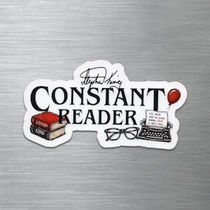 May include: A die-cut sticker featuring the text CONSTANT READER in black, with a signature above. Illustrations include a stack of two books, black-rimmed glasses, and a typewriter with a red balloon and text reading All work and no play makes Jack a dull boy.