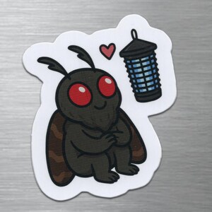 May include: A die-cut sticker featuring a cartoon moth with a dark gray body, large red eyes, and brown-patterned wings. The moth is positioned next to a small pink heart and a black bug zapper lantern with a blue grid pattern on a white background.