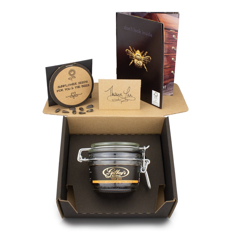 May include: A brown cardboard box with a black interior. The box contains a glass jar of honey labeled "Gilboy's Rose Gold", a small card with the text "Sunflower Seeds for You & The Bees", and a small card with the text "Thank You".