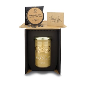 May include: A black gift box with a clear jar of honey inside. The jar has a gold lid and a gold label that says "Gilboy's Teign Valley HONEY 342g (12.1 oz)". The box also includes a small card with sunflower seeds and a thank you card.
