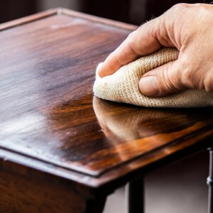 May include: A hand rubs a white cloth over a dark wood table top, polishing the surface to a shine.
