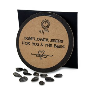 May include: A round, brown paper card with black trim and a sunflower illustration. The card says "Sunflower Seeds for You & The Bees".  A small pile of black sunflower seeds are scattered on a white surface.