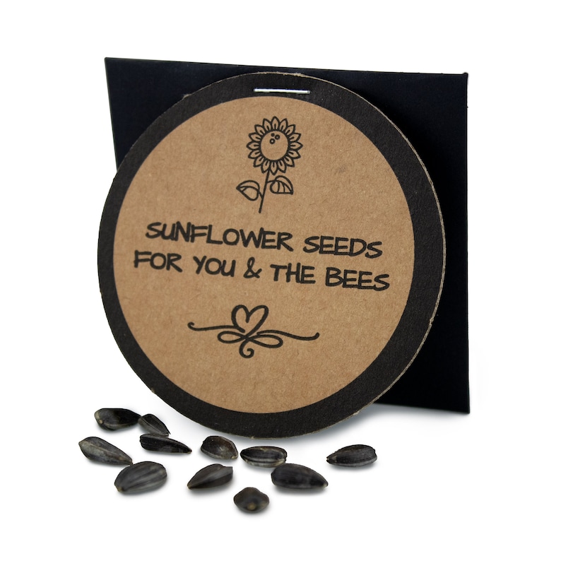 May include: A round, brown paper card with black trim and a sunflower illustration. The card says "Sunflower Seeds for You & The Bees".  A small pile of black sunflower seeds are scattered on a white surface.