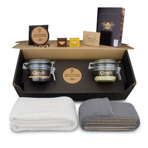 May include: A gift box with various items, including two glass jars with metal clasps, two rolled cloths, and small soaps. The box also contains a booklet with a bee illustration and the text "don't look inside."
