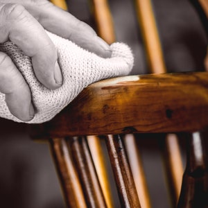 May include: A person's hand is using a white cloth to polish a wooden chair. The chair has a dark brown finish and is made of wood.