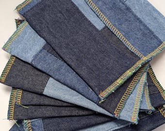 May include: A stack of denim coasters in various shades of blue. Each coaster is square with a patchwork design and a colorful stitched edge. The coasters are arranged in a fan shape, showcasing the different denim tones.