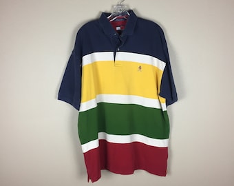 Könnte beinhalten: Ein mehrfarbiges, gestreiftes Poloshirt in den Farben Marineblau, Gelb, Grün, Weiß und Rot. Das Shirt hat ein kleines gesticktes Logo auf der linken Brust.