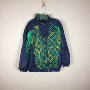 Puede incluir: Una chaqueta azul marino con un frente estampado en verde y amarillo. La chaqueta tiene una cremallera y un cuello alto.