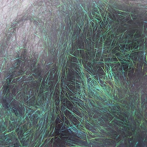 May include: Close-up of dark green craft material with iridescent highlights. The material appears to be made of thin, hair-like strands, creating a textured and shimmering effect. The strands are densely packed, giving the material a full appearance.