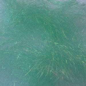 May include: Close-up of a mass of green, iridescent synthetic fibers. The fibers are long, thin, and have a slightly textured appearance. The color is a vibrant, sea-green hue with shimmering highlights.