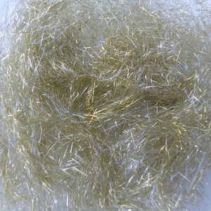 May include: Close-up of a mass of shiny, silver-colored tinsel. The tinsel strands are thin and create a dense, textured appearance. The light reflects off the strands, creating highlights and shadows. The overall effect is a shimmering, decorative material.