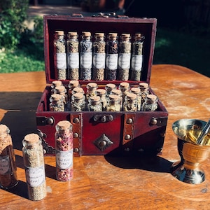 May include: A wooden chest filled with small glass bottles containing dried herbs and flowers. The chest has a brass latch and hinges. There is a small mortar and pestle made of brass on the table next to the chest.