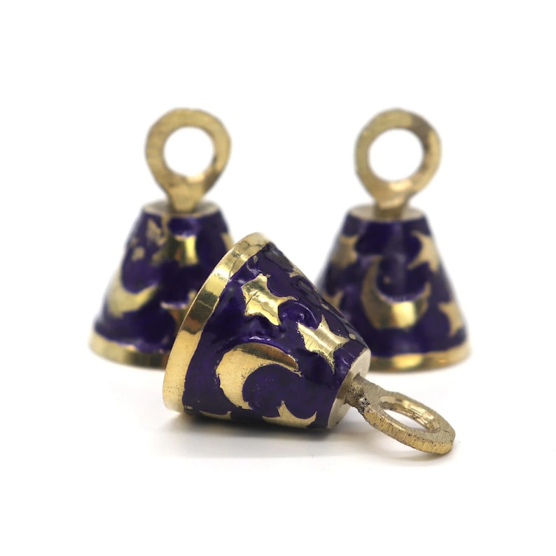 May include: Three small gold bells with purple enamel and gold crescent moon designs. The bells have a loop at the top for hanging.