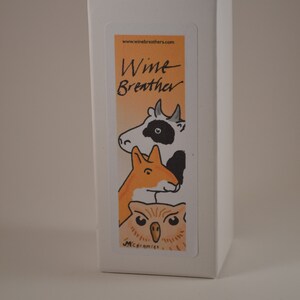 May include: White box with a colorful sticker featuring a cartoon cow, fox, and owl. The sticker says "Wine Breather" and "M.Ceramics" at the bottom.
