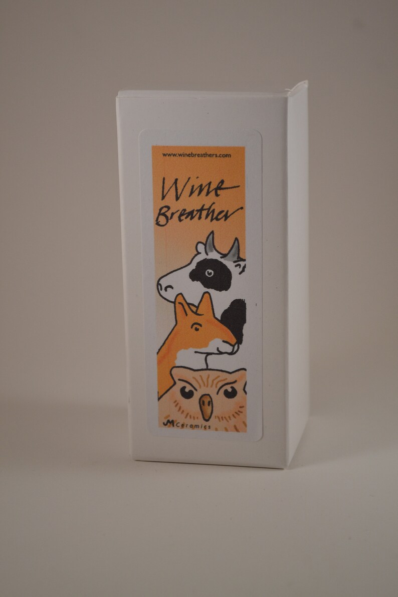 May include: White box with a colorful sticker featuring a cartoon cow, fox, and owl. The sticker says "Wine Breather" and "M.Ceramics" at the bottom.