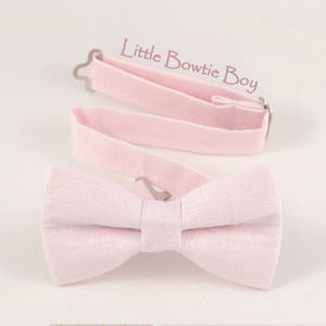 May include: A light pink bow tie with a matching adjustable neckband. The bow tie is made of a textured fabric and has a classic butterfly shape. The text "Little Bowtie Boy" is in the upper right corner.
