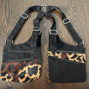 May include: Two black crossbody bags with adjustable straps and silver-tone hardware. One bag features a leopard print panel, while the other has a leopard print accent. Both have zippered pockets.