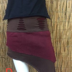 Puede incluir: Una falda asimétrica en marrón, burdeos y negro con un panel de malla. La falda tiene un aspecto desgastado con varios agujeros y bordes deshilachados.