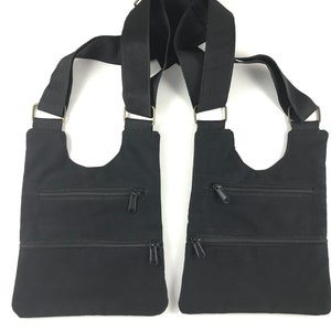 May include: Black canvas crossbody bag with two zippered pockets on each side. The bag has adjustable straps.