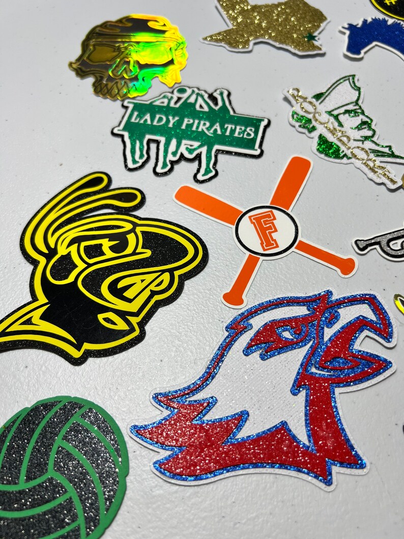 May include: Assortment of colorful iron-on patches with various designs, including a skull, a volleyball, a bird, a baseball bat, and a text that says "Lady Pirates".