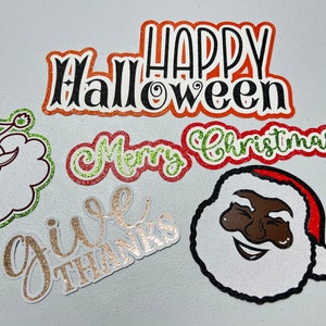 May include: Five glitter-covered paper cutouts with holiday greetings. The cutouts are in various colors, including red, green, gold, and black. The greetings are "Happy Halloween", "Merry Christmas", "Give Thanks", and a Santa Claus face.