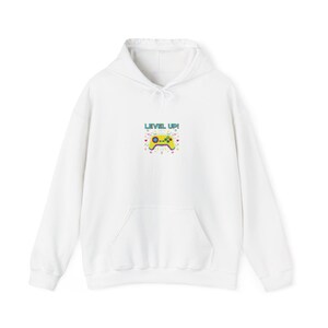 May include: White hoodie with a front pocket and drawstring hood. The front features a colorful graphic of a video game controller with the text "LEVEL UP!". The controller is yellow, with blue, red, and green accents.