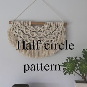 May include: A white macrame wall hanging with a half-circle pattern and fringe. The hanging is attached to a wooden dowel.