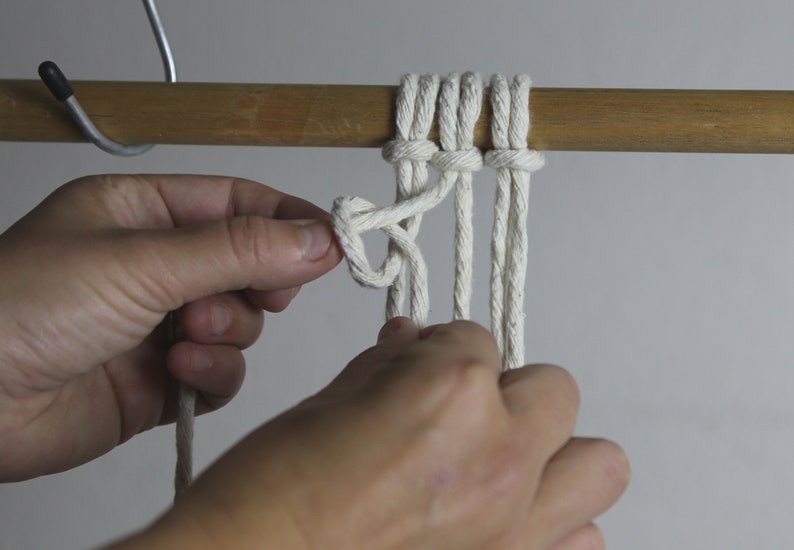 Pu&ograve; includere: Primo piano di una mano che fa un nodo a una corda bianca. La corda &egrave; avvolta attorno a un bastone di legno.