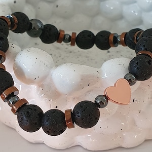 Op de afbeelding: Armband van zwarte lavasteen en koperen kralen met een rozen gouden hartbedel.