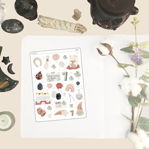May include: A sheet of stickers with a variety of good luck charms, including a horseshoe, a four-leaf clover, a rainbow, a dice, a wishbone, a lucky cat, and a ladybug. The stickers are in a variety of colors, including red, green, blue, and yellow. The text "Good Luck Spell" is included on one of the stickers.